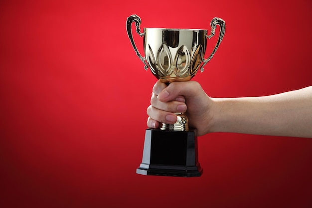 Abgeschnittene Hand einer Frau, die die Trophäe vor rotem Hintergrund hält
