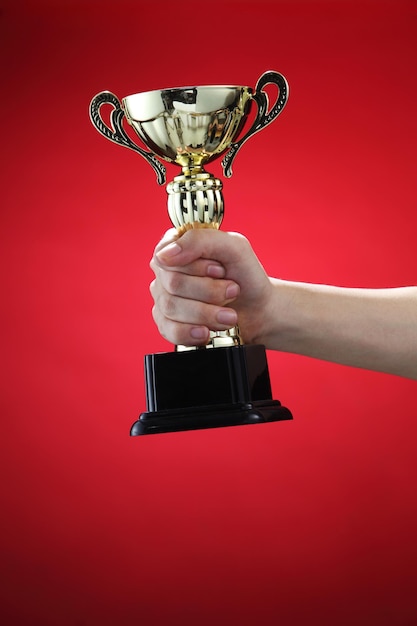 Abgeschnittene Hand einer Frau, die die Trophäe vor rotem Hintergrund hält