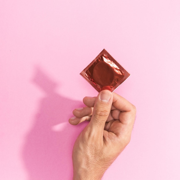 Abgeschnittene Hand einer Frau, die ein Geschenk vor rosa Hintergrund hält