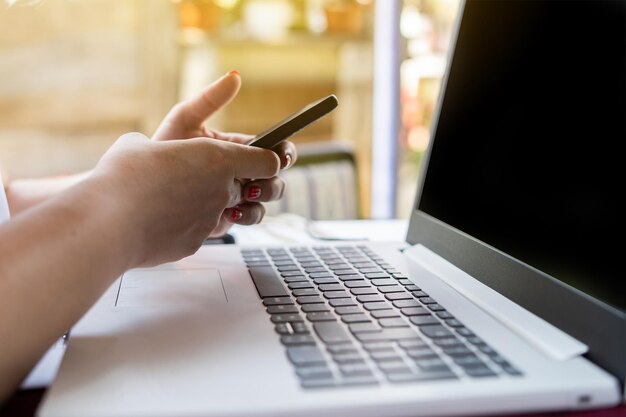 Foto abgeschnittene hand einer frau, die ein handy über einen laptop benutzt