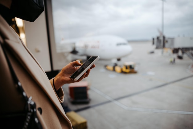 Foto abgeschnittene hand einer frau, die ein smartphone am flughafen benutzt