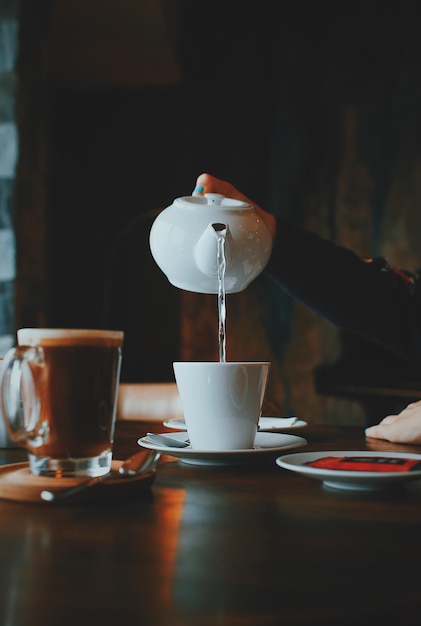 Abgeschnittene Hand einer Frau, die Wasser in Kaffee gießt