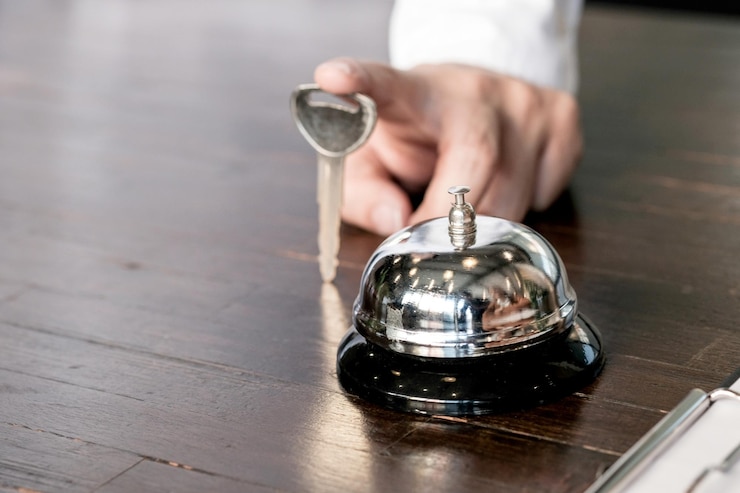 Foto abgeschnittene hand einer geschäftsperson, die den schlüssel an der dienstglocke auf einem holzschreibtisch im büro hält
