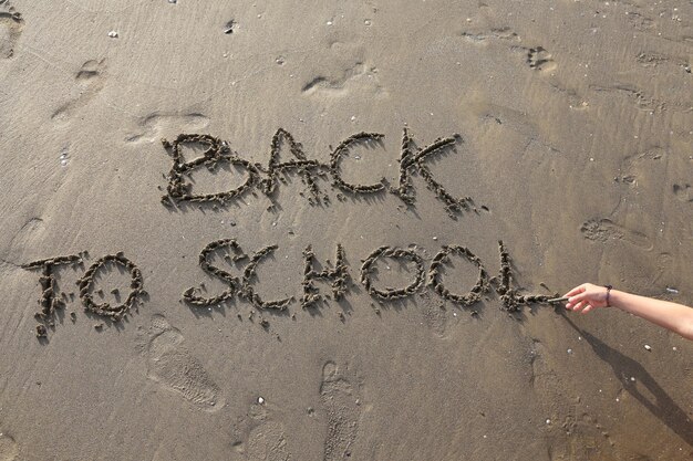 Abgeschnittene Hand einer Person, die am Strand Text auf Sand schreibt