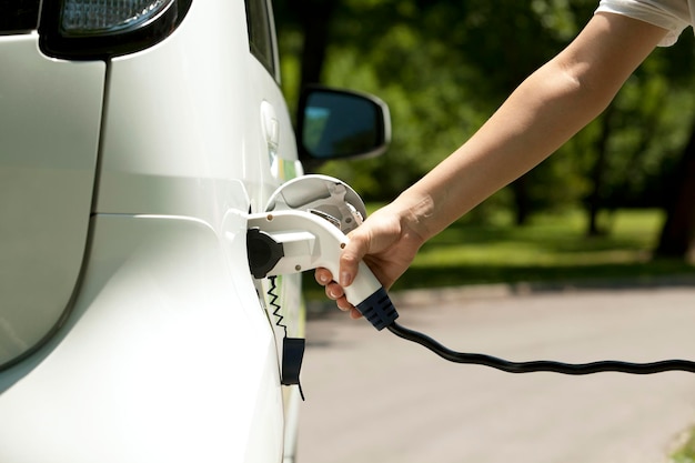 Abgeschnittene Hand einer Person, die ein weißes Elektroauto auflädt