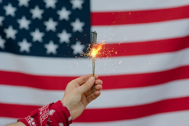 Abgeschnittene Hand einer Person, die leuchtende Funkeln gegen die amerikanische Flagge hält