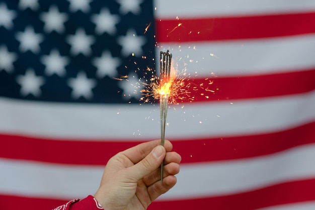 Abgeschnittene Hand einer Person, die leuchtende Funkeln gegen die amerikanische Flagge hält