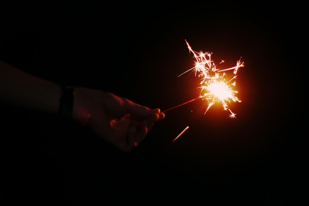 Abgeschnittene Hand einer Person, die nachts eine leuchtende Funkel hält