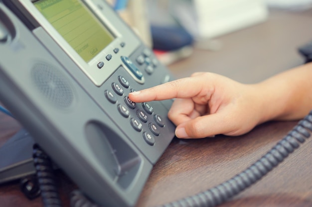 Abgeschnittene Hand einer Person, die Telefon-Tastatur auf dem Tisch wählt