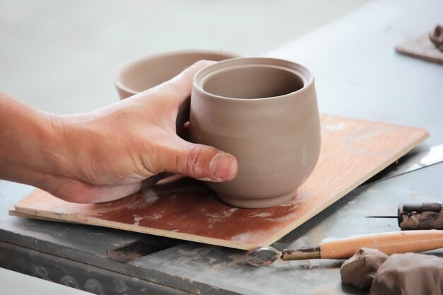 Abgeschnittene Hand einer Person, die Töpferwaren auf dem Tisch hält