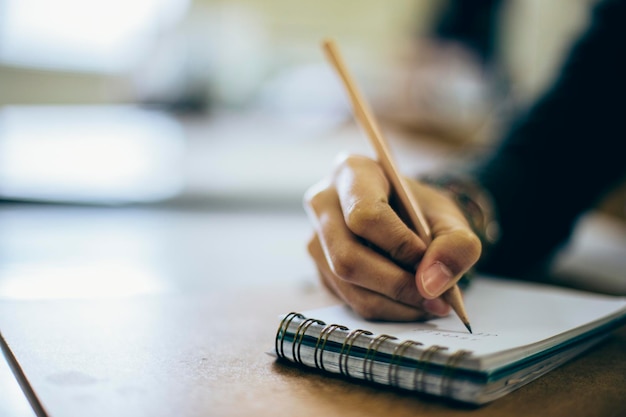 Abgeschnittene Hand einer weiblichen Studentin, die auf einem Schreibblock auf dem Schreibtisch schreibt