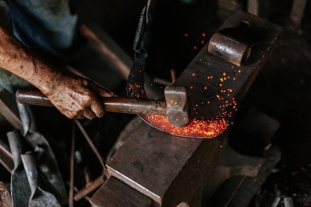 Abgeschnittene Hand eines Arbeiter, der in einer Fabrik auf geschmolzenes Metall schlägt
