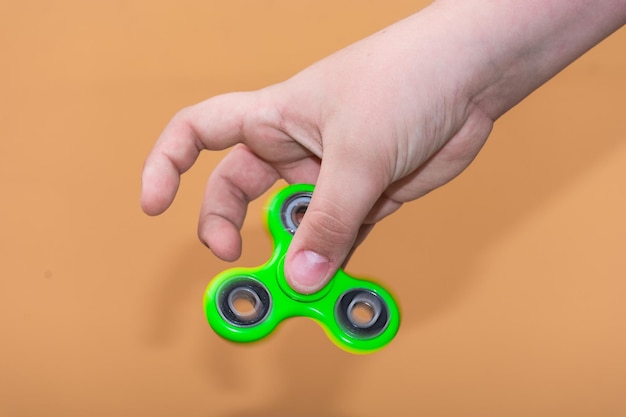 Abgeschnittene Hand eines Jungen, der einen Spinner gegen einen farbigen Hintergrund hält