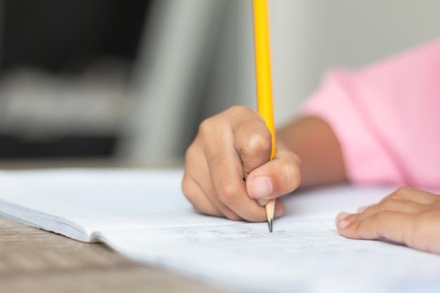 Abgeschnittene Hand eines Kindes, das mit Bleistift auf ein Buch schreibt