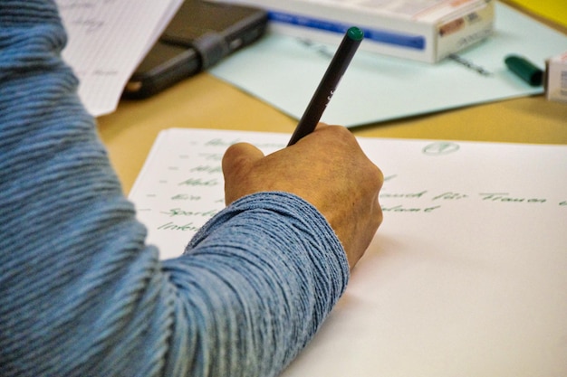 Foto abgeschnittene hand eines mannes, der auf einem schreibtisch auf papier schreibt