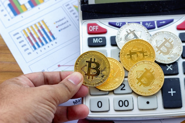 Abgeschnittene Hand eines Mannes, der Bitcoin mit Rechner auf dem Tisch hält