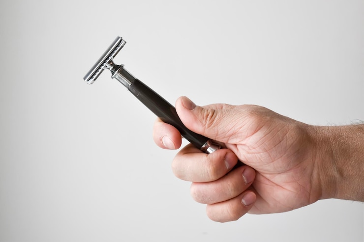 Foto abgeschnittene hand eines mannes, der ein rasiermesser über einem grauen hintergrund hält