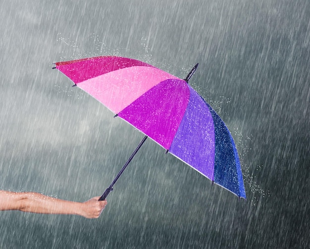 Foto abgeschnittene hand eines mannes, der während des regens einen regenschirm hält