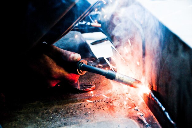 Foto abgeschnittene hand eines schweißers, der metall in der fabrik schweißt