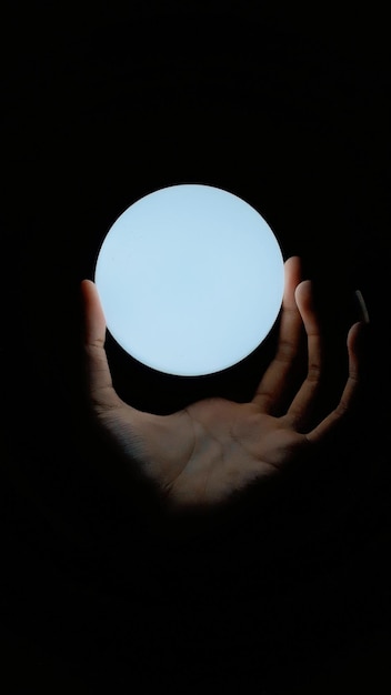 Foto abgeschnittene hand hält eine beleuchtete glühbirne im dunkelraum