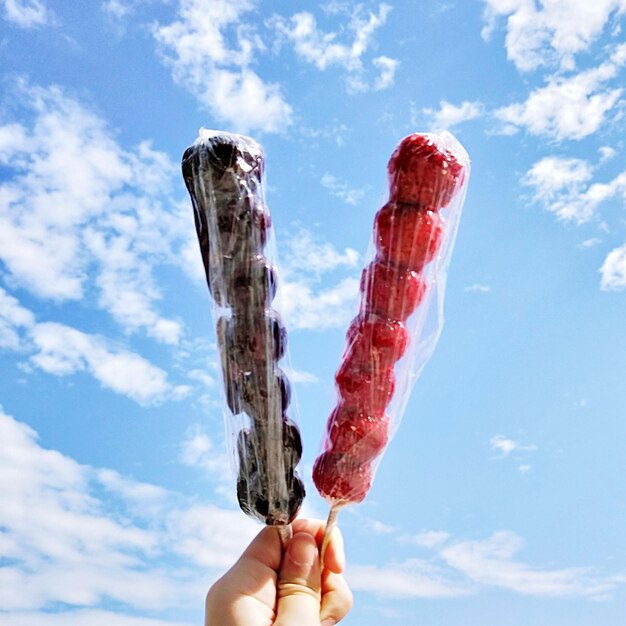 Abgeschnittene Hand hält süßes Essen gegen den blauen Himmel