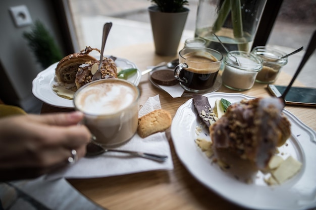 Foto abgeschnittene hand mit kaffee und dessert auf dem tisch