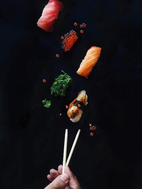 Abgeschnittene Hand mit Sushi mit Essstäbchen auf schwarzem Hintergrund