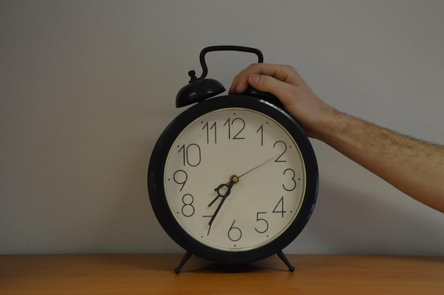 Abgeschnittene Hand über Wecker auf dem Tisch gegen die Wand