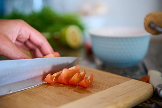 Foto abgeschnittener blick auf einen koch, der rote, saftige tomaten auf einem holzbrett schneidet
