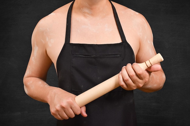 Abgeschnittener Blick auf einen männlichen Koch mit einer Walze auf schwarzem Hintergrund, der einen Walze für den Teig hält