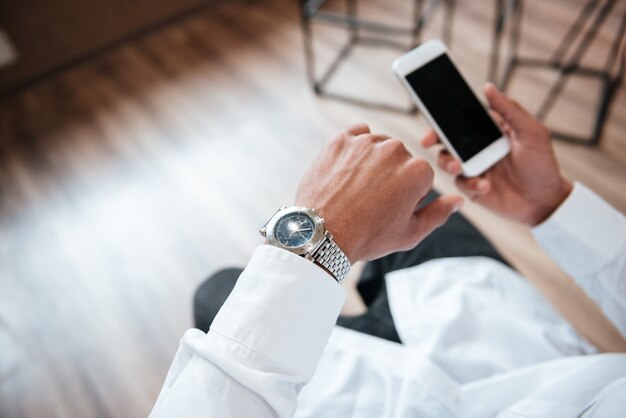 Abgeschnittener gutaussehender Geschäftsmann, der im Büro per Telefon chattet, schaut auf die Uhr