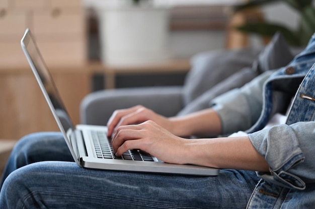 Abgeschnittener junger Mann, der mit Laptop-Computer im Internet surft, während er auf der Couch sitzt