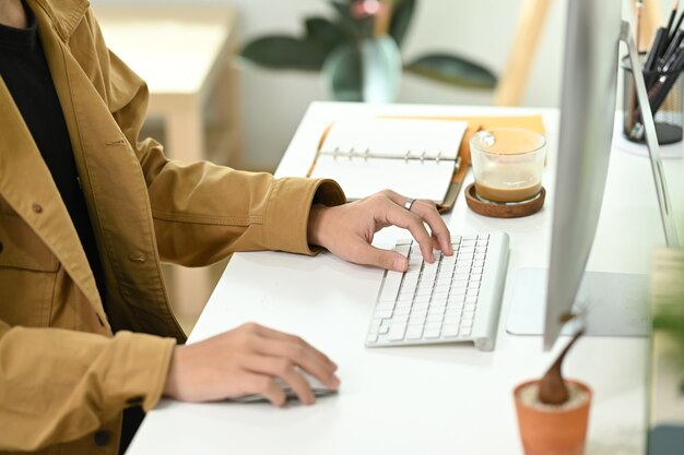 Abgeschnittener Schussgeschäftsmann, der an einem modernen Arbeitsplatz sitzt und mit Computer arbeitet.