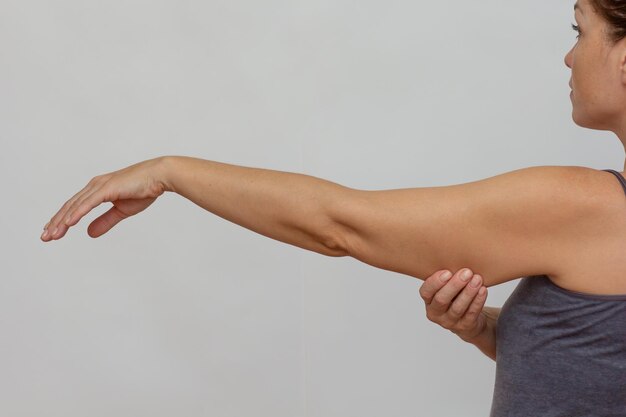 Foto abgeschnittener weiblicher körper zeigt einen arm mit hängender haut auf grauem hintergrund