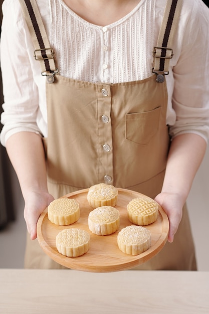 Abgeschnittenes Bild einer Frau, die ein Holztablett mit Mondkuchen hält, die bereit sind, im Ofen gebacken zu werden