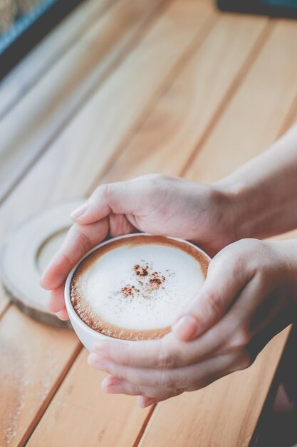 Foto abgeschnittenes bild einer frau, die eine kaffeetasse über dem tisch hält