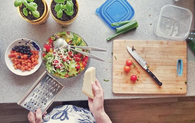 Foto abgeschnittenes bild einer frau, die käse über salat in der küche reibt