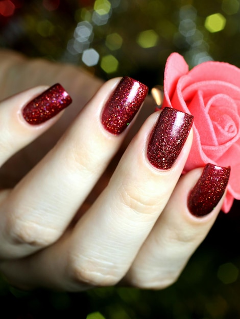 Abgeschnittenes Bild einer Frau mit roter Nagellackhand, die eine künstliche Rose hält