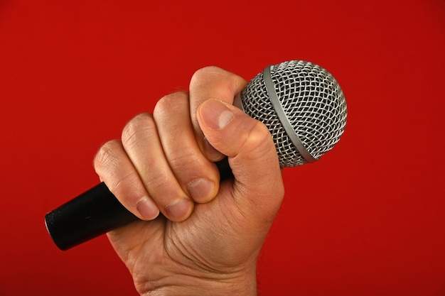 Abgeschnittenes Bild einer Hand, die ein Mikrofon vor rotem Hintergrund hält
