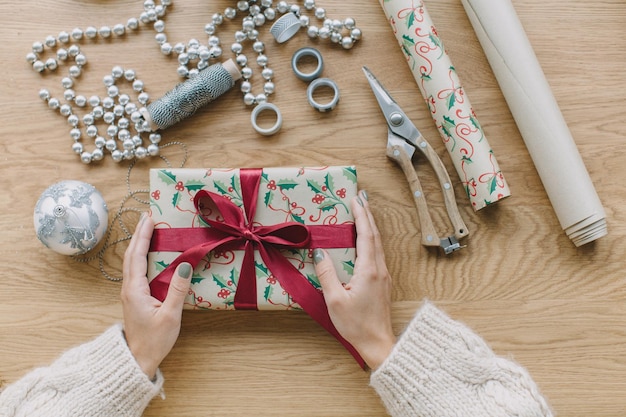Foto abgeschnittenes bild einer hand, die ein weihnachtsgeschenk auf dem tisch hält