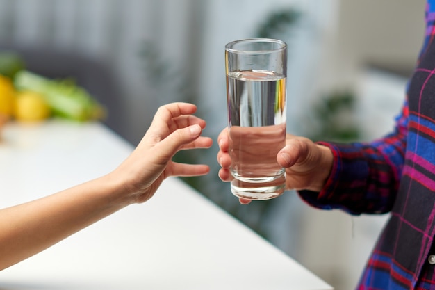 Abgeschnittenes Bild einer Hand eines kleinen Mädchens, die ein Glas Wasser in der Küche mit der jungen Mutter hält.