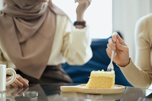 Abgeschnittenes Bild einer jungen Frau, die Diätkuchen isst und mit einer Freundin im Café spricht