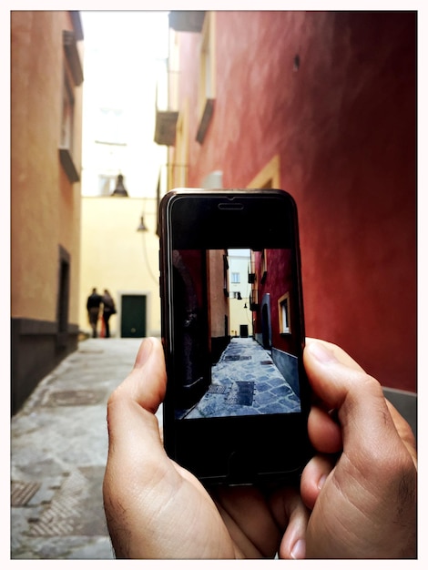 Abgeschnittenes Bild einer Person, die eine Gasse inmitten von Gebäuden fotografiert