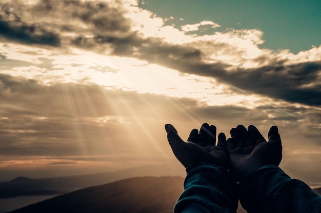 Abgeschnittenes Bild einer Person mit gekuppelten Händen gegen einen bewölkten Himmel bei Sonnenuntergang