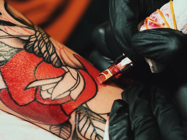 Abgeschnittenes Bild einer weiblichen Künstlerin, die ein Tattoo auf der Hand eines männlichen Kunden macht