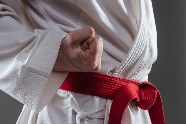 Abgeschnittenes Bild eines gutaussehenden Sportlers in Kimono-Praxis in Karate und Geste mit Hand einzeln auf grauem Hintergrund.