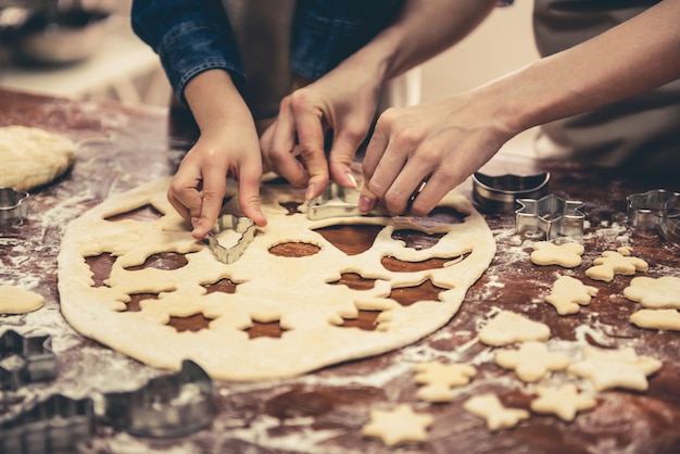 Abgeschnittenes Bild eines kleinen Mädchens und ihrer Mutter in Schürzen, die Kekse mit Ausstechformen in der Küche zubereiten