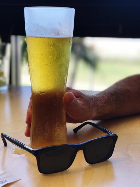 Foto abgeschnittenes bild eines mannes, der bier mit sonnenbrille auf dem tisch trinkt