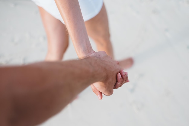 Abgeschnittenes Bild eines Paares, das sich an den Händen hält, während es am Strand spazieren geht