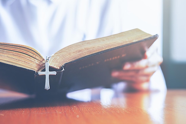 Abgeschnittenes Bild eines Priesters, der an einem Tisch die Bibel liest